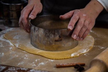 Hamur katmanı fırın kağıdının üzerinde yatıyor, kek kalıbı da metal kesiciyle kesiliyor..