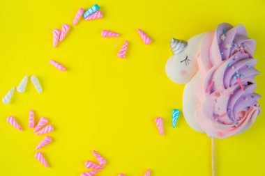 Bizet tek boynuzlu atı beyaz pembe-mor kuyruklu ve gümüş boynuzlu parlak sarı arka planda yatar, çok renkli boynuzları dairenin etrafına saçılmıştır.