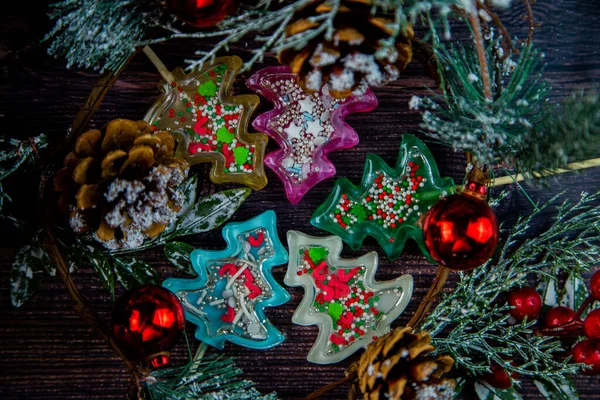 Noel ağacının dalları, koniler ve Noel oyuncaklarıyla çevrili ahşap bir masanın üzerinde farklı renklerde lolipoplardan oluşan bir sürü Noel ağacı bulunur..
