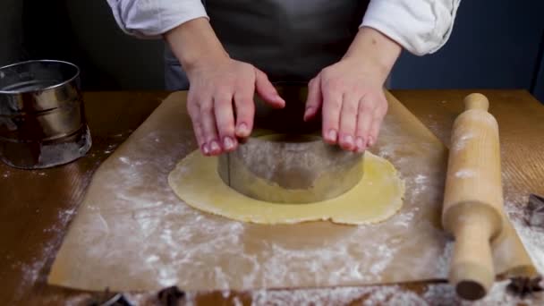 The rolled out layer of dough lies on dark parchment in flour surrounded by a rolling pin and an iron flour cup. A circle is cut out of the dough with an iron mold, excess dough is removed, then — стоковое видео