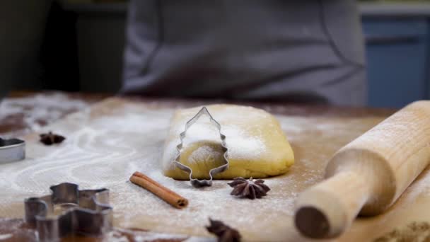 Sur un parchemin sombre dans la farine, il y a un bloc de pâte, sur lequel repose un coupe-biscuits en forme d'arbre de Noël, un rouleau à pâtisserie, d'autres moules, de la cannelle et des clous de girofle, blanc — Video