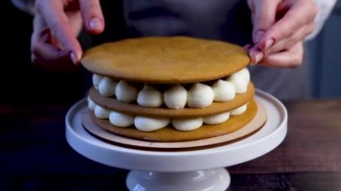 On the cake, which is decorated with white cream and red raspberry jam, the pastry chef puts the cake on top and presses on it with his hand to hold it tighter.