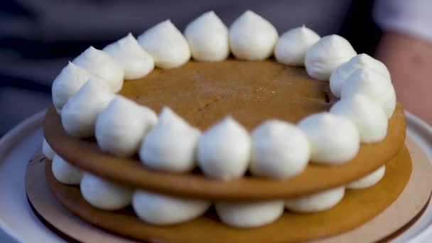 On dark honey cakes, which are decorated with circles of white cream around the edges, cream is applied from a pastry bag to the center, making a small inner circle. — Stockvideo