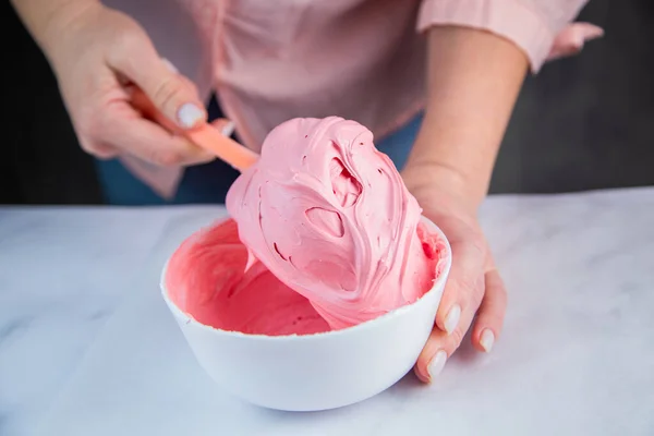 Pink confectionary meringue marengo is mixed in a white bowl on a white marble background by the hands of a pastry chef — Stock Photo, Image