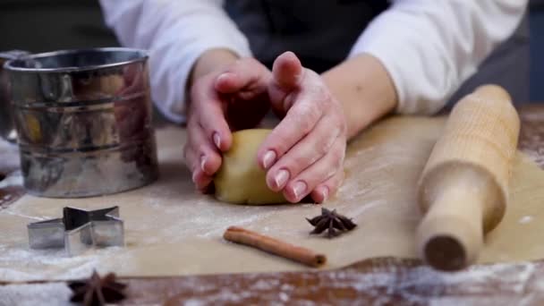 Le pâtissier lisse la pâte avec ses mains, la tord et la tourne dans le sens des aiguilles d'une montre, la transformant en une pâte plus plate. Moules, farine, rouleau à pâtisserie et cannelle sont visibles du côté. — Video