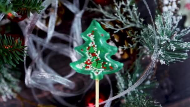 Lollipop in the form of Christmas trees - rattle shaking from side to side, inside the balls are moving on the background of a Christmas tree — Stock Video