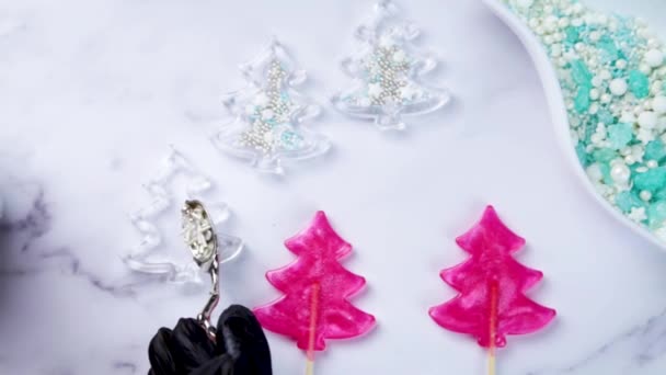 Een meester in zwarte handschoenen giet losse snoepjes in karamel, voor het maken van een snoeprammelaar in de vorm van een kerstboom, tegen een achtergrond van wit marmer. — Stockvideo