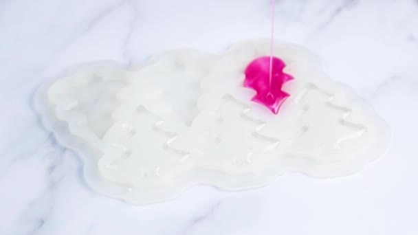 O caramelo rosa é derramado em um molde de silicone branco com um fluxo fino, um molde na forma de árvores de Natal, contra um fundo de mármore branco. — Vídeo de Stock