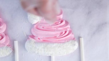 Beyaz ponponları ve kenarları olan pembe kremalı şapkaların kenarında beyaz toplar serpiştiriliyor, parşömen arka planına karşı.