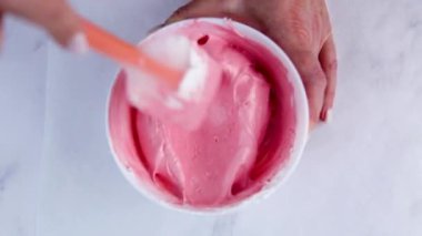Bir spatulayla yemek pişirmek beyaz bir kasede pembe krema karıştırır.