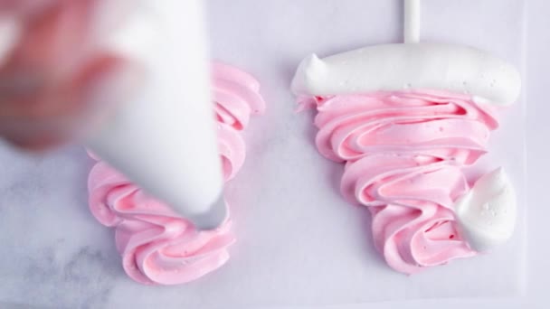 Op licht perkament zijn er roze meringue caps op stokjes, de kok maakt een pompon en een franje van een banketbakje van witte meringue. — Stockvideo