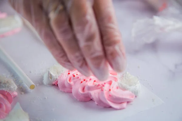 Beyaz ponponları ve kenarları olan pembe kremalı şapkaların kenarında beyaz toplar serpiştiriliyor, parşömen arka planına karşı.