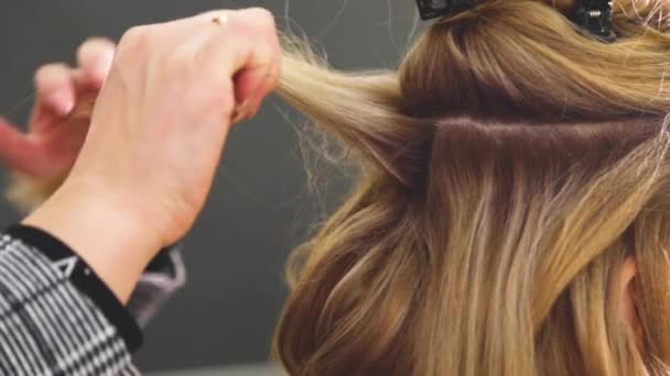 Um fio de cabelo é levantado, pulverizado com verniz e, em seguida, penteado com um pente, e cachos são feitos com um ferro de cabelo. — Vídeo de Stock