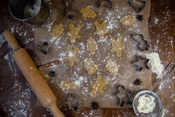 Auf dem Pergament liegen fertige Kekse in verschiedenen Formen, Nudelholz, Ausstechformen und ein Sieb mit Mehl liegen daneben, Mehl ist überall verstreut. — Stockfoto