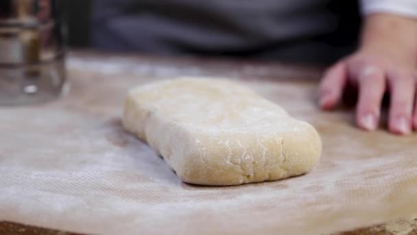 Le cuisinier utilise un cutter à partir d'un gros morceau de pâte couché sur un parchemin saupoudré de farine, sépare une partie et la ramasse. Gros plan vidéo et dans une touche sombre — Video