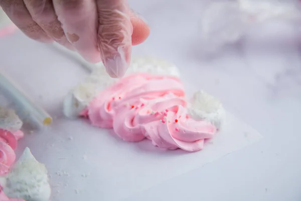 Beyaz ponponları ve kenarları olan pembe kremalı şapkaların kenarında beyaz toplar serpiştiriliyor, parşömen arka planına karşı.