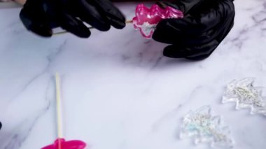 Şeker Noel ağaçlarının pembe rengini yapan siyah eldivenli bir usta, karameli açık arkaplan boyunca birbirine bağlar.