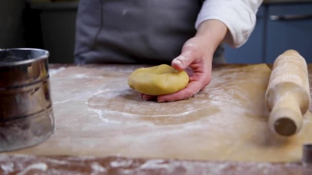 O chefe de pastelaria segura a massa nas mãos, polvilhe-a com farinha, depois limpa-a com farinha, coloca-a no pergaminho e mexe-a. Vídeo na tecla escura — Vídeo de Stock
