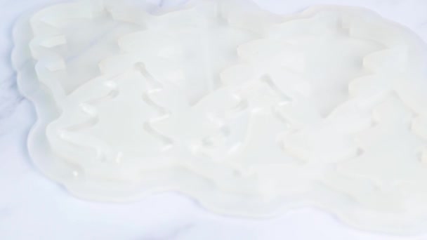 Průhledný karamel se nalije do bílé silikonové formy s tenkým potůčkem, plísní v podobě vánočních stromků, na pozadí z bílého mramoru — Stock video