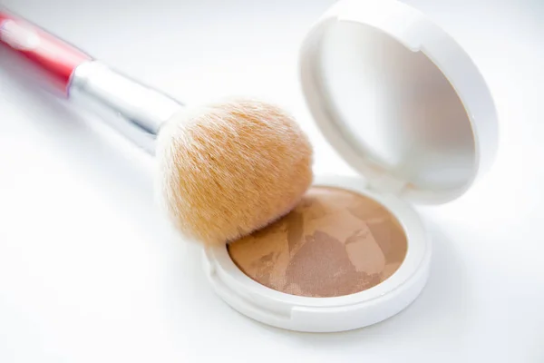 A white pillbox with powder and bronzer lies on a white background, on it lies a brush for blush on top. Stock Image