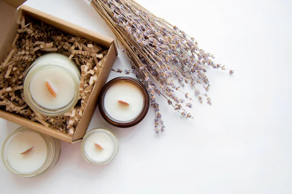 An open box with candles on a white background, next to it are several candles in a jar and a dried bouquet of lavender.