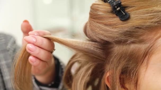 Una hebra de cabello castaño claro se peina con un peine y luego se enrosca en rizos con una plancha para el cabello — Vídeos de Stock