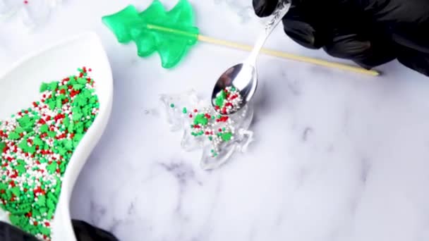 Мастер в черных перчатках наливает конфеты в карамель, чтобы сделать погремушку в виде рождественской елки, на фоне белого мрамора. — стоковое видео