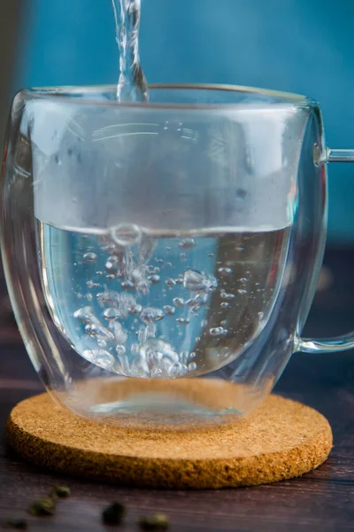 Hot water is poured into a transparent mug on a wooden stand, bubbles in the water.