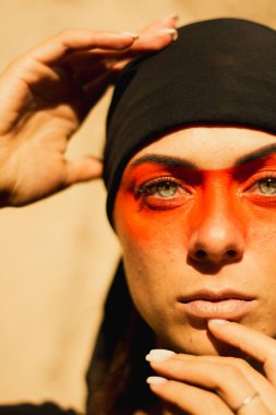 Portrait of a young beautiful woman with makeup and face art in American tribal or Middle Eastern style. Ethnic image, red eyes and black headscarf. Close-up.