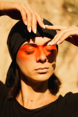 Portrait of a young beautiful woman with makeup and face art in American tribal or Middle Eastern style. Ethnic image, red eyes and black headscarf. Close-up.
