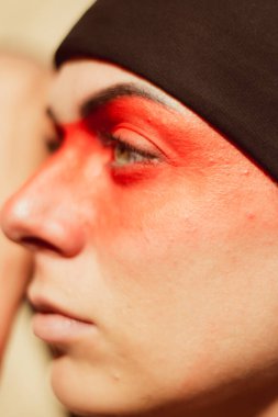 Portrait of a young beautiful woman with makeup and face art in American tribal or Middle Eastern style. Ethnic image, red eyes and black headscarf. Close-up.