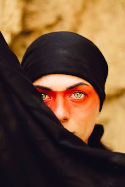 Makyajlı ve yüz sanatıyla Amerikan kabilesi ya da Orta Doğu tarzında güzel bir kadının portresi. Etnik imaj, kırmızı gözler ve siyah başörtüsü. Yakın plan..