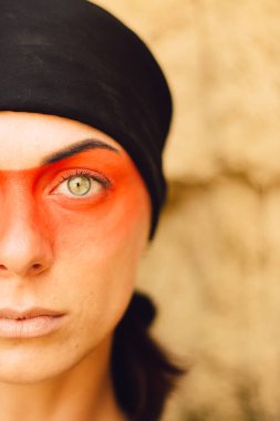 Portrait of a young beautiful woman with makeup and face art in American tribal or Middle Eastern style. Ethnic image, red eyes and black headscarf. Close-up.
