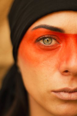 Makyajlı ve yüz sanatıyla Amerikan kabilesi ya da Orta Doğu tarzında güzel bir kadının portresi. Etnik imaj, kırmızı gözler ve siyah başörtüsü. Yakın plan..