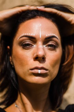 Portrait of a young beautiful woman with makeup and white face art ornament in american tribal or middle eastern style. Ethnic image Close-up on the background of a sandy wall.