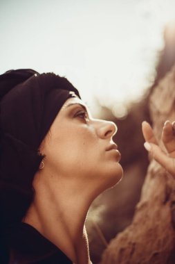 Makyajlı, beyaz yüzlü, kabile ya da orta doğu tarzında siyah tesettüre bürünmüş güzel bir kadının portresi. Kumlu bir duvarın arka planında etnik görüntü.