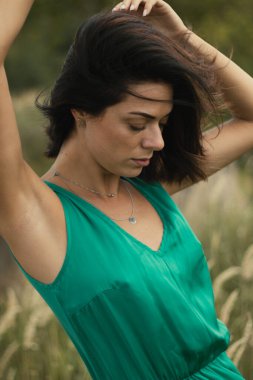 Açık havada özel dersler. Yeşil çayır üzerinde yeşil elbiseli genç esmer, yeşil tarlası olan bir köyde doğal makyajlı güzel bir kız. Doğal güneş ışığı yaz güneşli gün