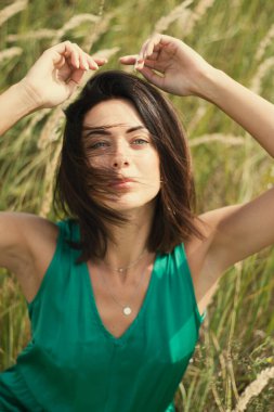 Açık havada özel dersler. Yeşil çayır üzerinde yeşil elbiseli genç esmer, yeşil tarlası olan bir köyde doğal makyajlı güzel bir kız. Doğal güneş ışığı yaz güneşli gün
