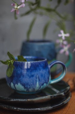 Seramik bardak koyu mavi, açık mavi ve nane renginde buruşmuş. Gri ve ahşap arka plan. Tasarımın için bir yer.