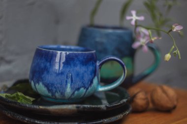 Seramik bardak koyu mavi, açık mavi ve nane renginde buruşmuş. Gri ve ahşap arka plan. Tasarımın için bir yer.