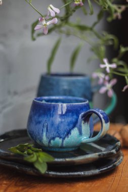 Seramik bardak koyu mavi, açık mavi ve nane renginde buruşmuş. Gri ve ahşap arka plan. Tasarımın için bir yer.