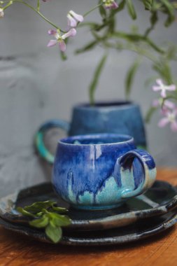 Seramik bardak koyu mavi, açık mavi ve nane renginde buruşmuş. Gri ve ahşap arka plan. Tasarımın için bir yer.