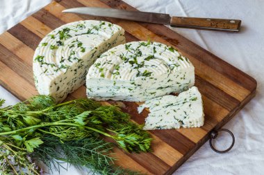 Tahta bir sürahinin yanında baharatlı otlarla ev yapımı organik beyaz peynir dilimlenmiş. Doğal ışık, güzel arkaplan ve tasarımın için yer var.