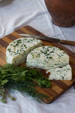 Tahta bir sürahinin yanında baharatlı otlarla ev yapımı organik beyaz peynir dilimlenmiş. Doğal ışık, güzel arkaplan ve tasarımın için yer var.