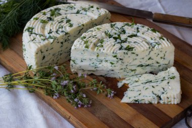 Tahta bir sürahinin yanında baharatlı otlarla ev yapımı organik beyaz peynir dilimlenmiş. Doğal ışık, güzel arkaplan ve tasarımın için yer var.