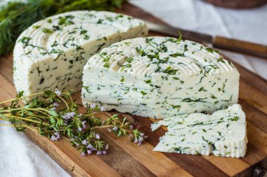 Tahta bir sürahinin yanında baharatlı otlarla ev yapımı organik beyaz peynir dilimlenmiş. Doğal ışık, güzel arkaplan ve tasarımın için yer var.
