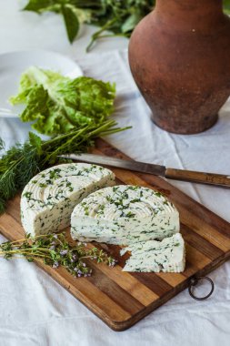 Tahta bir sürahinin yanında baharatlı otlarla ev yapımı organik beyaz peynir dilimlenmiş. Doğal ışık, güzel arkaplan ve tasarımın için yer var.