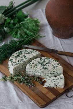 Tahta bir sürahinin yanında baharatlı otlarla ev yapımı organik beyaz peynir dilimlenmiş. Doğal ışık, güzel arkaplan ve tasarımın için yer var.