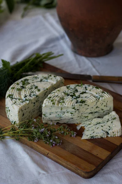 Tahta bir sürahinin yanında baharatlı otlarla ev yapımı organik beyaz peynir dilimlenmiş. Doğal ışık, güzel arkaplan ve tasarımın için yer var.
