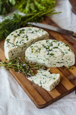 Tahta bir sürahinin yanında baharatlı otlarla ev yapımı organik beyaz peynir dilimlenmiş. Doğal ışık, güzel arkaplan ve tasarımın için yer var.